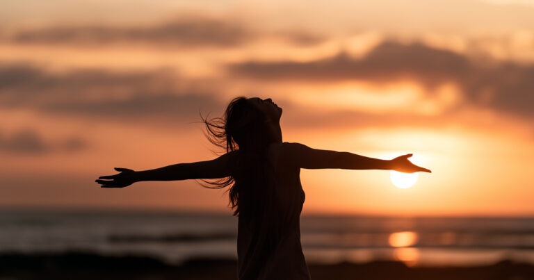 Silhouette of woman holding her arms out at sunset