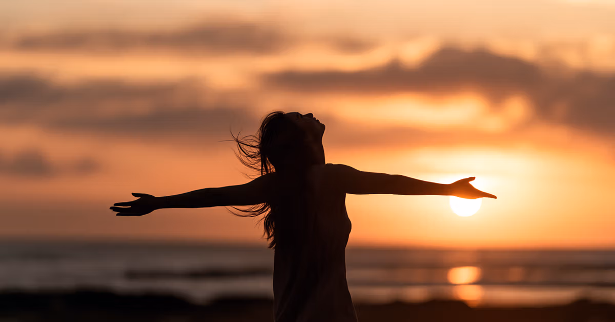 Silhouette of woman holding her arms out at sunset